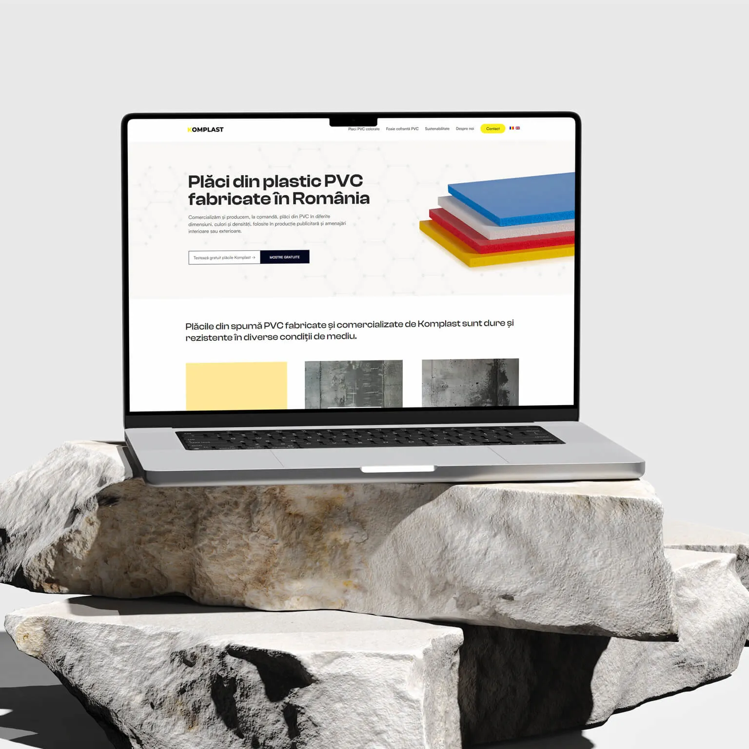 Pagina principală a site-⁠ului Komplast pe laptop, cu teancul de plăci PVC colorate