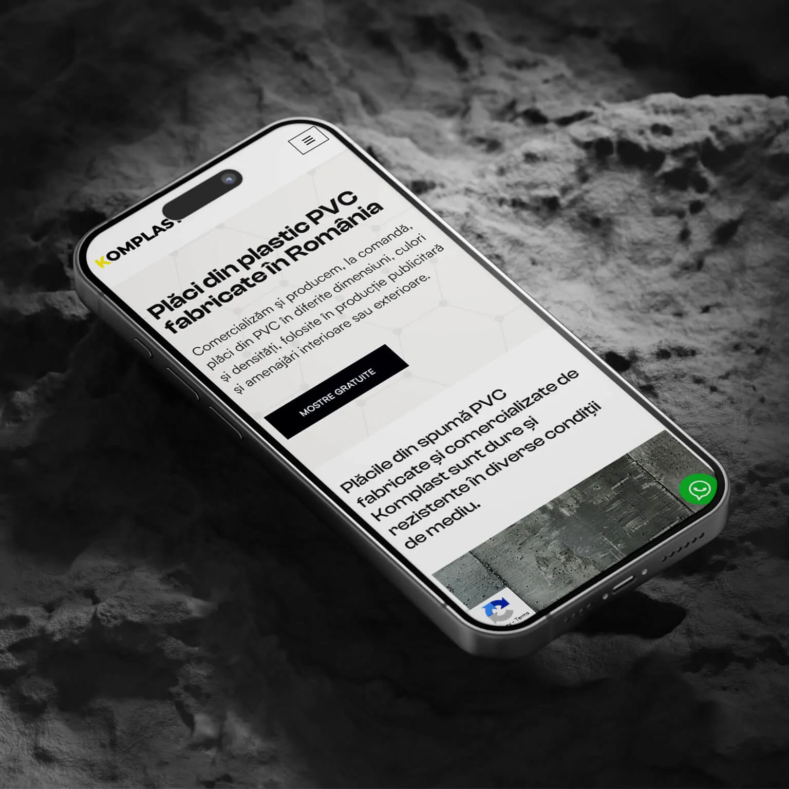 Pagina principală a site-⁠ului Komplast pe un telefon așezat pe o suprafață de piatră